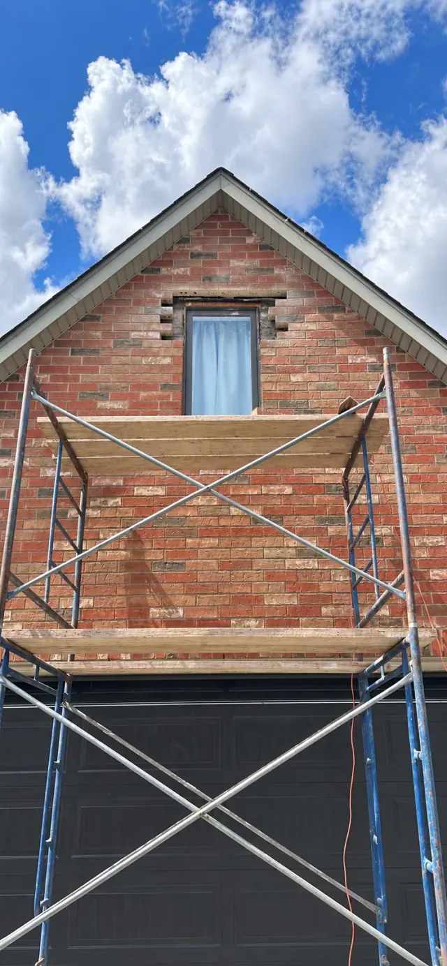 Brick removed around an upper-storey gable window, with the opening exposed behind scaffolding