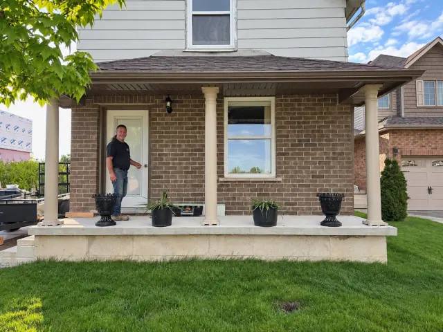 Brown brick facade behind three porch columns and a concrete landing
