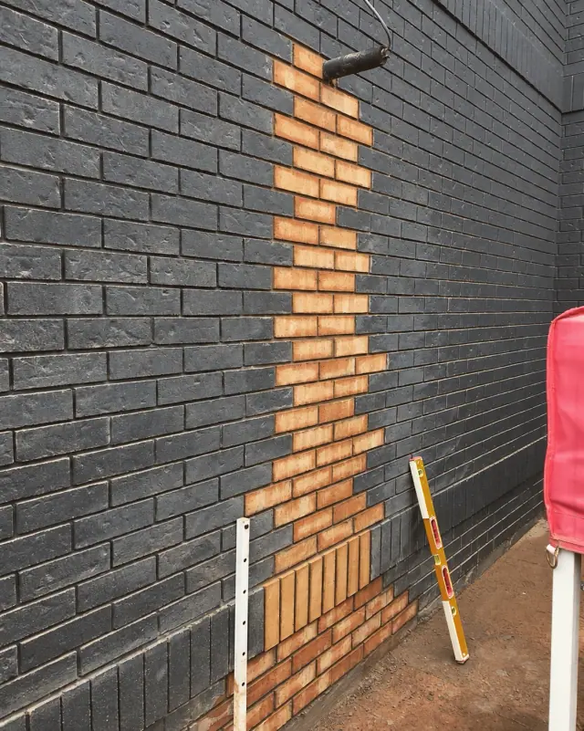 Unpainted orange brick infill in a dark brick wall, with tools alongside