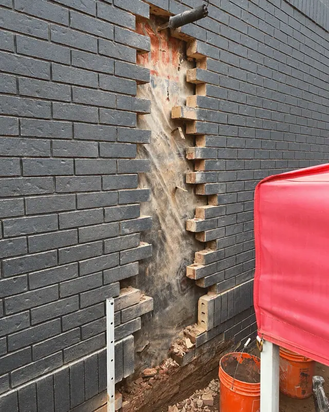 A vertical opening in a dark brick wall, showing exposed backing and toothed brick edges