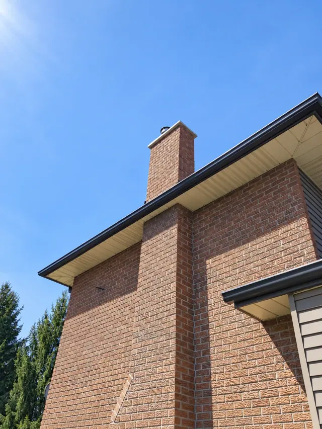 Completed brick chimney and cap above the roof, viewed from the side of the house