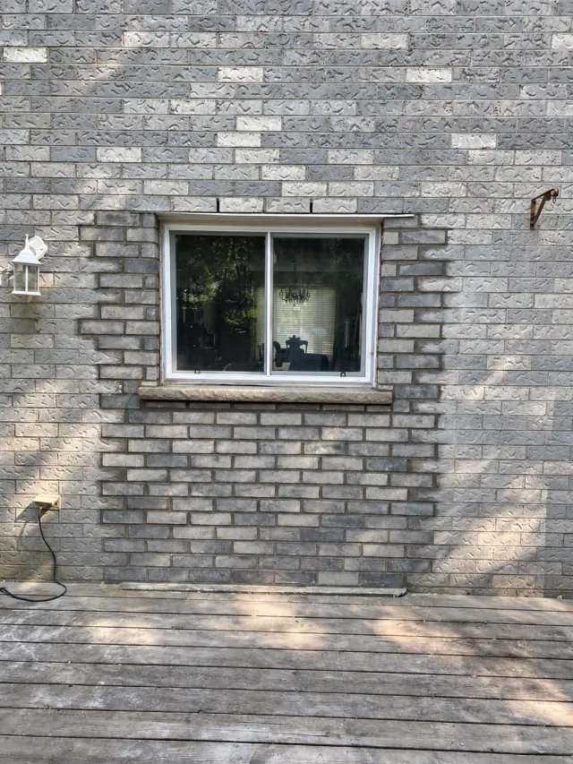 Grey brickwork and mortar around a white-framed window above a timber deck