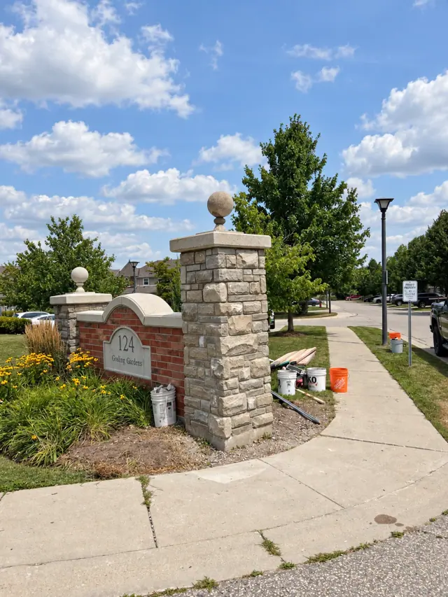Stone entrance pillars with round finials beside a brick sign and planted border