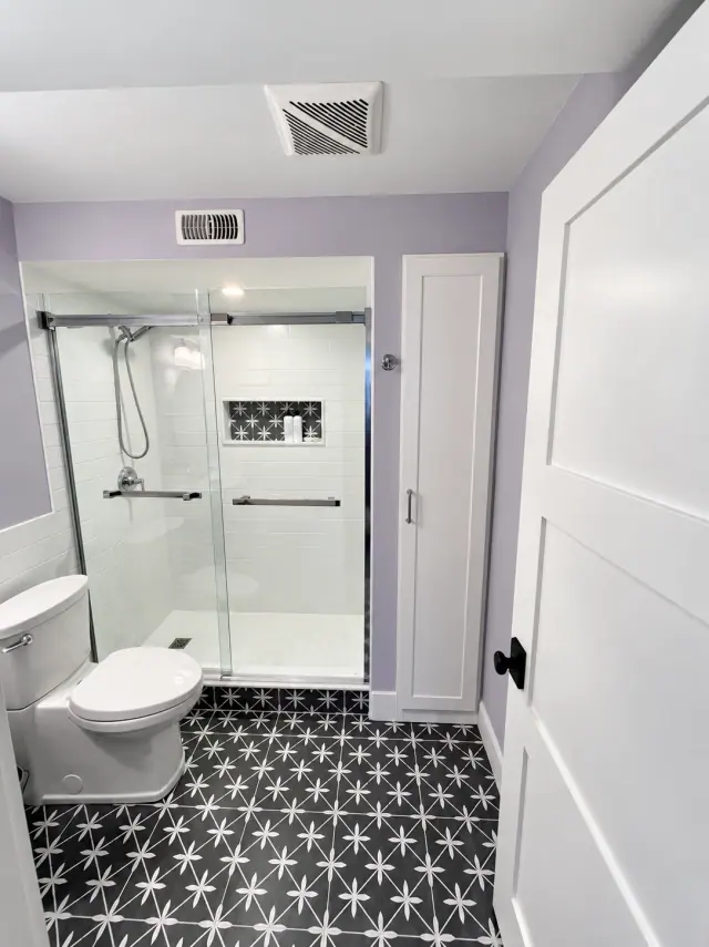 Black and white patterned floor tile, white shower walls and a matching patterned niche behind a glass screen