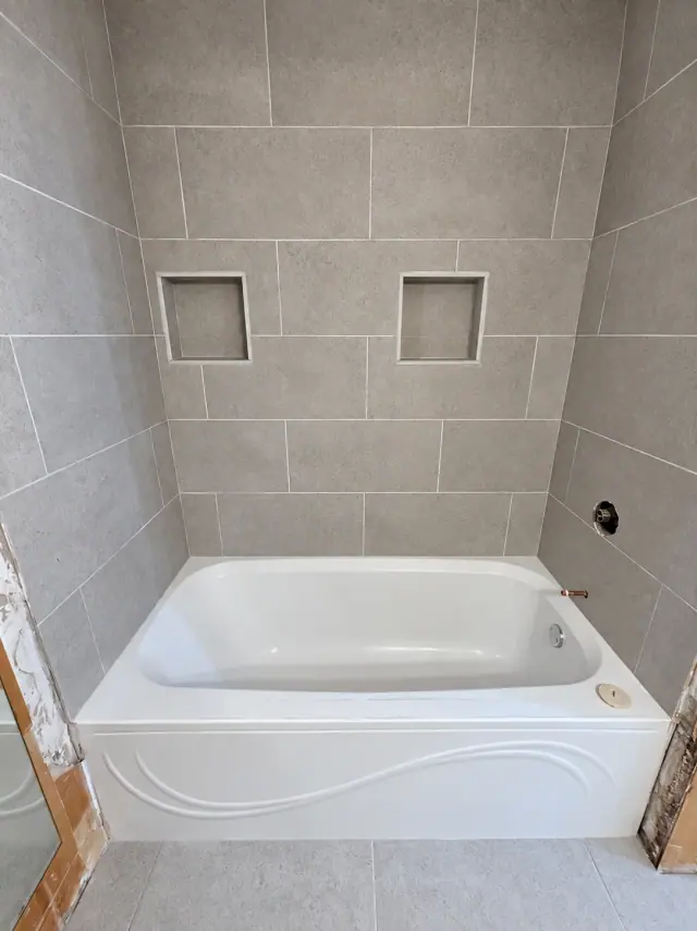 Grey rectangular tile and two recessed niches around a white bathtub