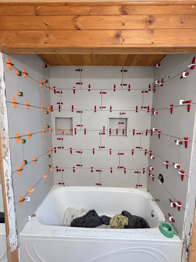 Grey wall tiles held by leveling clips around a bathtub, with open joints before grouting